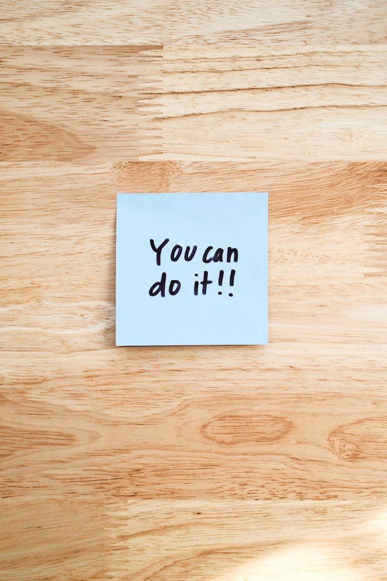 A motivational message on a Post-It note placed on a wooden table.