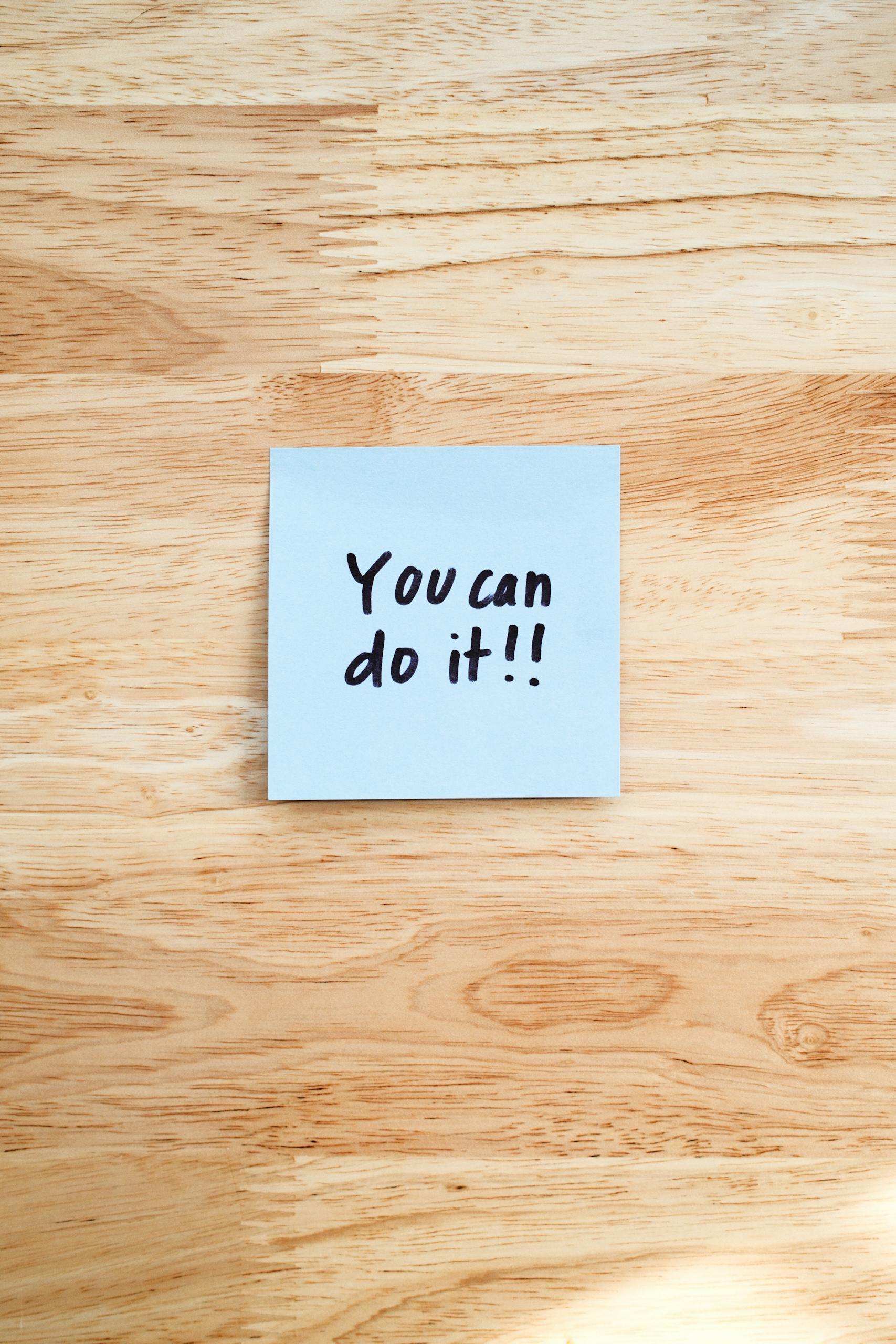 A motivational message on a Post-It note placed on a wooden table.